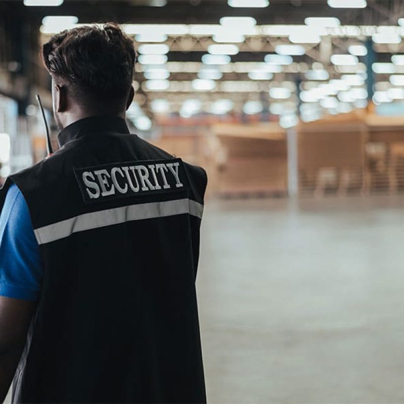 Security guard wearing a vest labeled ‘SECURITY’ patrols a large warehouse